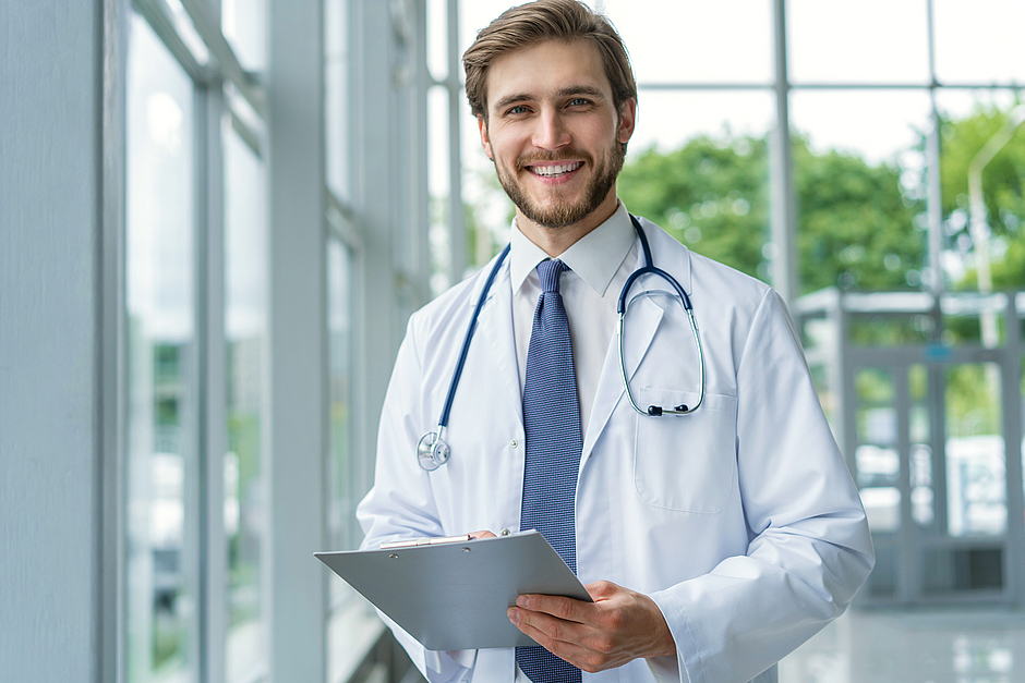 Ärzt*in in Weiterbildung steht auf dem Klinikflur und schaut in die Kamera